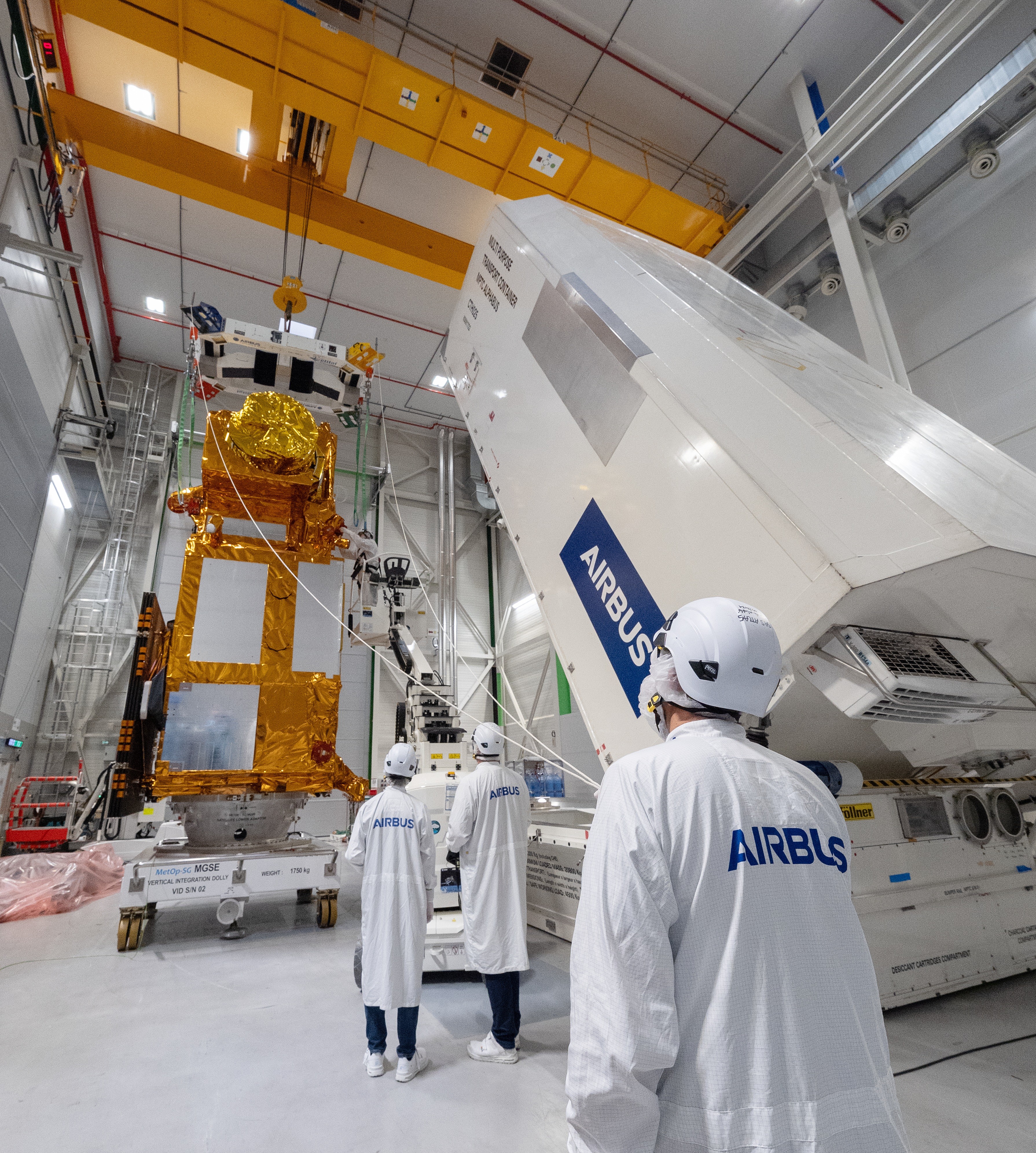 Покрытый золотистым материалом MetOp-SG-B1, специалисты и транспортный контейнер на предприятии Airbus.